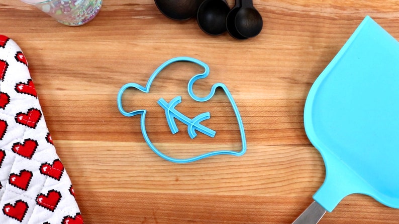 May include: A blue plastic cookie cutter shaped like a leaf with a small leaf design inside. The cutter is on a wooden surface.