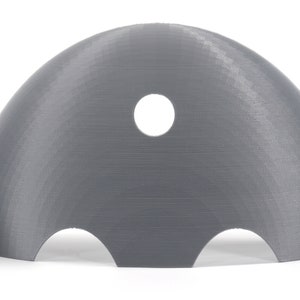May include: A gray plastic dome with a hole in the top and three cutouts on the bottom. The dome is designed to be used as a mold for creating objects.