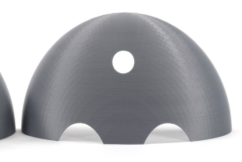 May include: A gray plastic dome with a hole in the top and three cutouts on the bottom. The dome is designed to be used as a mold for creating objects.