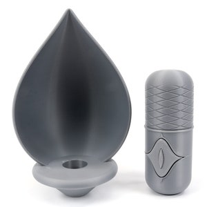 May include: A gray 3D printed candle holder shaped like a teardrop with a round base and a small hole in the center. Next to it is a gray 3D printed cylindrical container with a textured pattern and a small eye-shaped design.