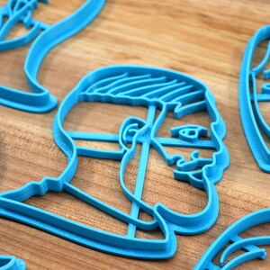 Op de afbeelding: Een set blauwe plastic koekjesvormen in de vorm van gezichten. De vormen liggen op een houten oppervlak.