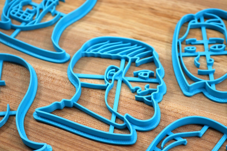 Op de afbeelding: Een set blauwe plastic koekjesvormen in de vorm van gezichten. De vormen liggen op een houten oppervlak.