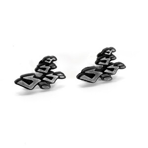 May include: A pair of silver-colored earrings with a black outline in the shape of the "ZA WARUDO" symbol from the anime series JoJo's Bizarre Adventure.