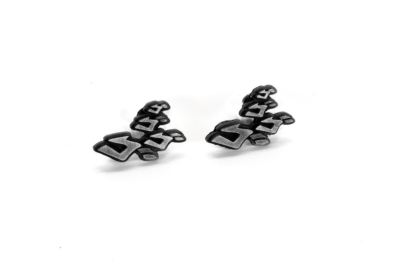 May include: A pair of silver-colored earrings with a black outline in the shape of the "ZA WARUDO" symbol from the anime series JoJo's Bizarre Adventure.