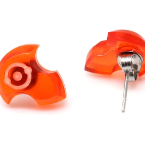 May include: A pair of orange resin earrings with silver posts. The earrings are shaped like a stylized heart.