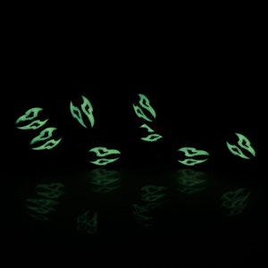 May include: A set of eight glow-in-the-dark dice with a black and green color scheme. The dice are scattered on a black surface and are reflecting light.