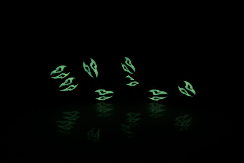 May include: A set of eight glow-in-the-dark dice with a black and green color scheme. The dice are scattered on a black surface and are reflecting light.
