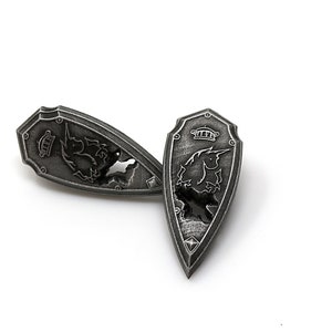 May include: Two silver-toned metal shield-shaped pins with a unicorn design. The unicorn is facing left on one pin and right on the other. The pins are on a white background.