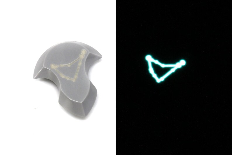 May include: A gray ceramic tile with a white outline of the constellation Capricorn. The tile glows green in the dark.