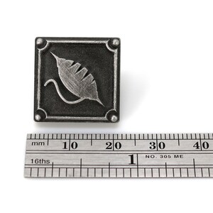 May include: A silver metal square with a stylized leaf design. The square is approximately 1.5 inches wide.