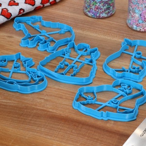 May include: Five blue plastic cookie cutters shaped like different animals. The cutters are on a wooden surface.