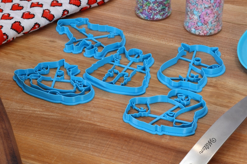 May include: Five blue plastic cookie cutters shaped like different animals. The cutters are on a wooden surface.
