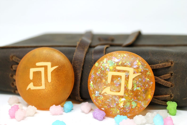May include: Two round, orange resin bookmarks with a white kanji character on each. The bookmarks are on a brown leather journal with a leather strap.