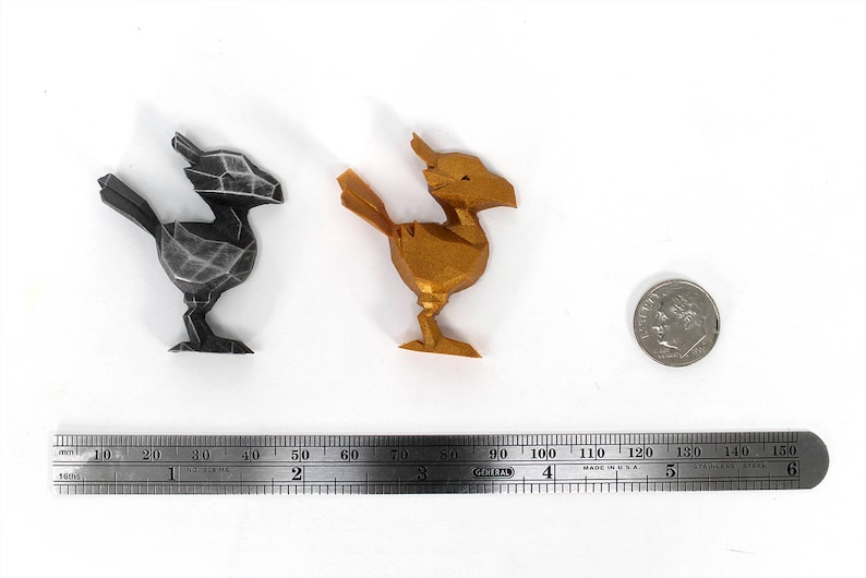 May include: Two 3D printed figurines of a mythical creature, one in black and one in gold. The figurines are about 5 cm tall and are sitting on a white surface. A ruler is in the background.
