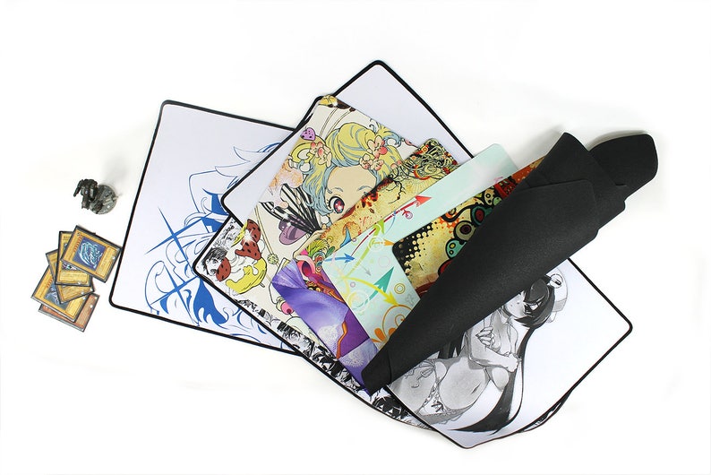 May include: A stack of colorful mousepads with various anime and graphic designs. The mousepads are on a white surface. One mousepad is rolled up and has a black surface.