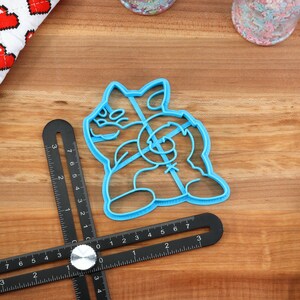 May include: A blue plastic cookie cutter shaped like a cartoon dog. The cutter is on a wooden surface.