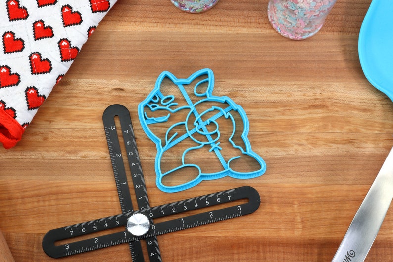 May include: A blue plastic cookie cutter shaped like a cartoon dog. The cutter is on a wooden surface.