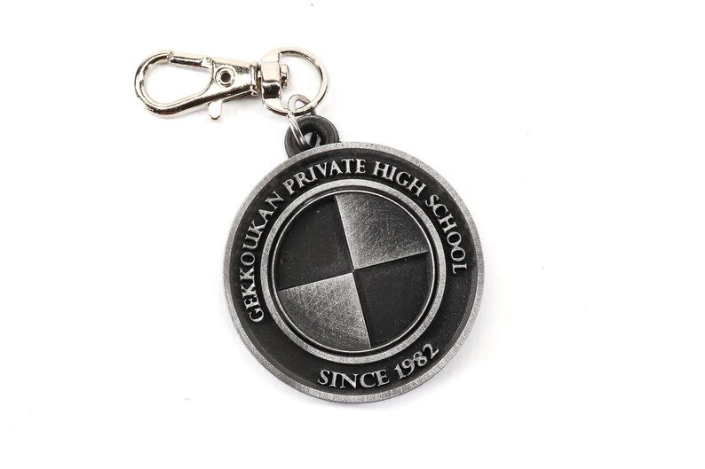 May include: A silver keychain with a round charm featuring the text "Gekkoukan Private High School Since 1982" and a black and silver quartered circle design.