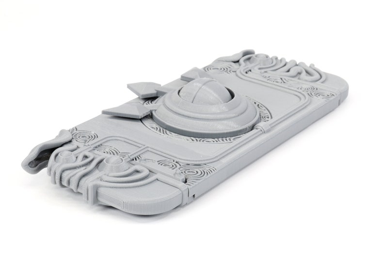 May include: A gray 3D printed case for a Nintendo Switch console. The case features an intricate design with a circular opening on the top.