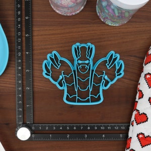 May include: Blue plastic cookie cutter shaped like a cartoon monster with three arms and a toothy grin.