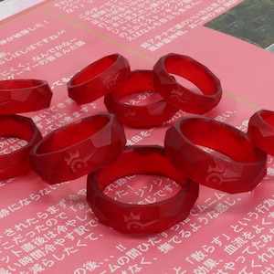 May include: A group of ten red resin rings with a geometric design and a raised symbol on each ring.