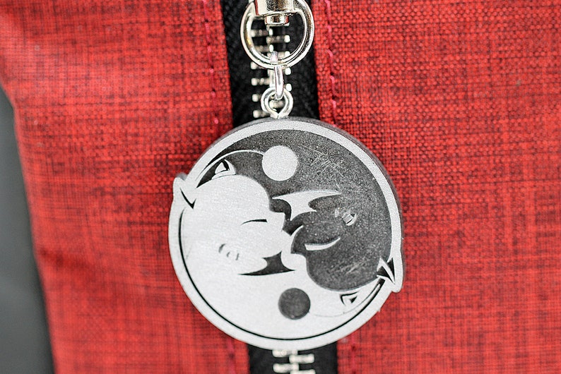 May include: A silver yin yang charm with a black and white design of two animals facing each other. The charm is attached to a silver zipper pull.