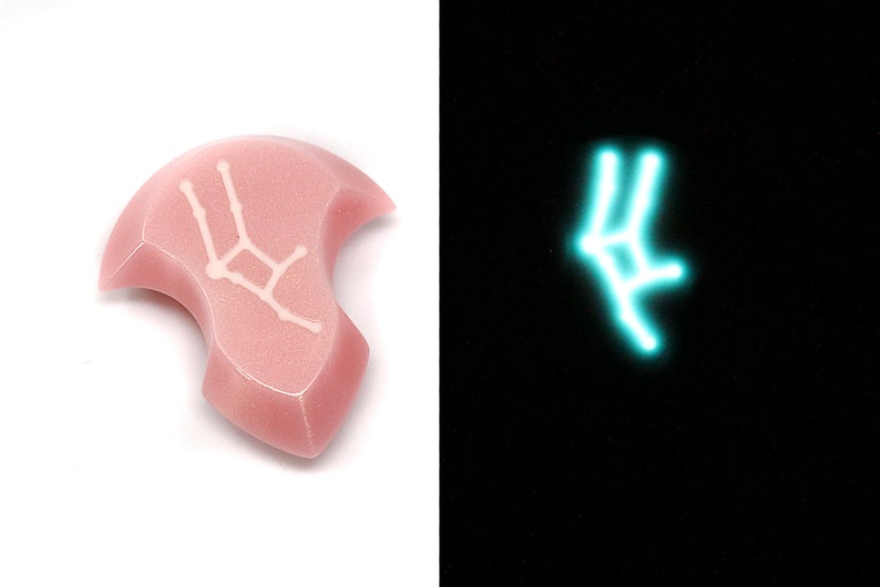 May include: A pink ceramic pendant with a white outline of the Gemini constellation. The pendant glows a light blue in the dark.