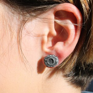 May include: A close-up of a person's ear with a silver earring featuring a circular design.