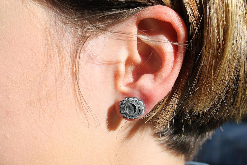 May include: A close-up of a person's ear with a silver earring featuring a circular design.