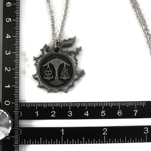 May include: A silver necklace with a pendant featuring a stylized symbol with a scale design and two smaller symbols. The pendant is about 2 inches in diameter.
