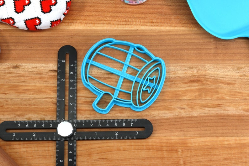 Puede incluir: Cortador de galletas de pl&aacute;stico azul en forma de tambor con una estrella en el lateral. El cortador est&aacute; sobre una superficie de madera con una regla.