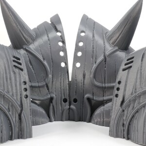 May include: Four gray 3D printed helmets with horns, each with a unique design and intricate details. The helmets are arranged in a circle, with the horns pointing outwards.