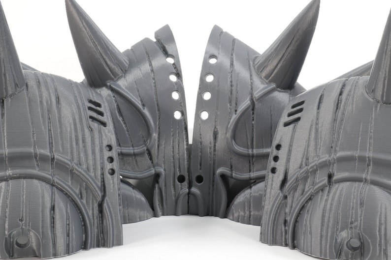 May include: Four gray 3D printed helmets with horns, each with a unique design and intricate details. The helmets are arranged in a circle, with the horns pointing outwards.