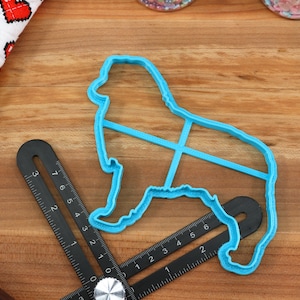 May include: A blue plastic cookie cutter shaped like a dog. The cutter is on a wooden surface with a ruler.