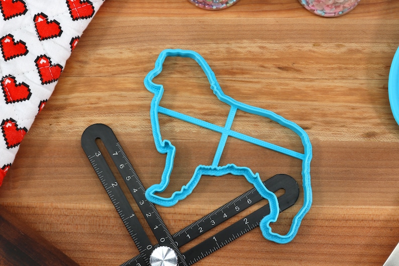 May include: A blue plastic cookie cutter shaped like a dog. The cutter is on a wooden surface with a ruler.