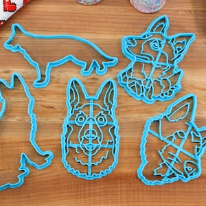 May include: Set of five blue plastic cookie cutters shaped like German Shepherd dogs. The cutters include a full body, a head, and three different head variations.