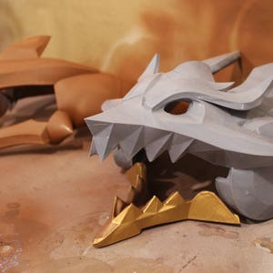 May include: A gray and gold dragon head costume piece with sharp teeth and a textured surface.