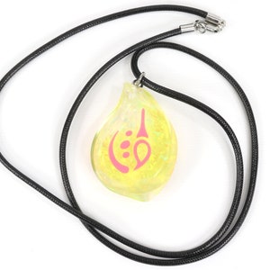 May include: A yellow teardrop-shaped pendant necklace with a pink symbol on it. The necklace is made of black cord.