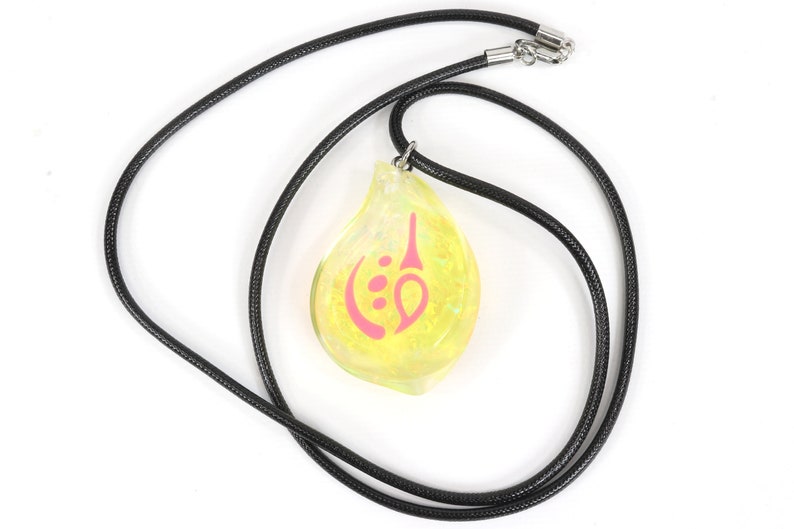 May include: A yellow teardrop-shaped pendant necklace with a pink symbol on it. The necklace is made of black cord.