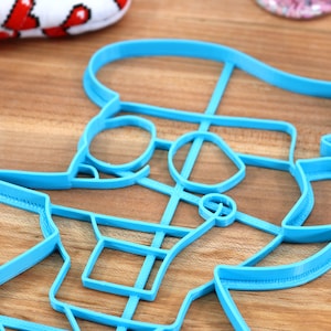 May include: A blue plastic cookie cutter shaped like a cartoon character with a hat and glasses.