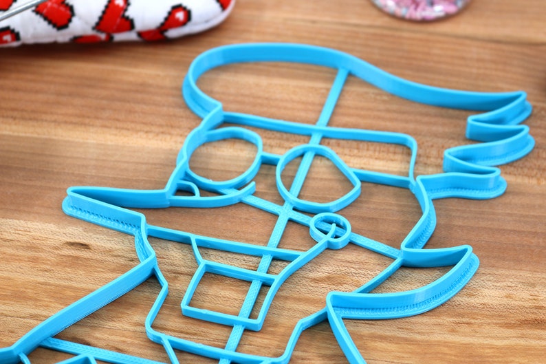 May include: A blue plastic cookie cutter shaped like a cartoon character with a hat and glasses.