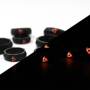 May include: A set of black silicone rings with a red swirl design. The rings glow in the dark, with the swirl design visible in the dark.