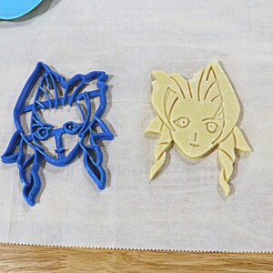 May include: Two cookie cutters, one blue and one yellow, shaped like a woman's face with long hair.