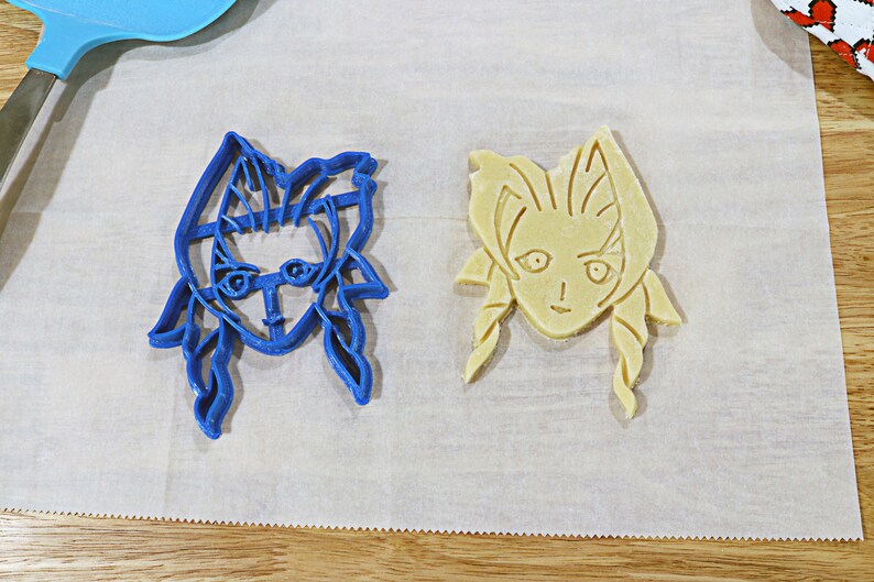 May include: Two cookie cutters, one blue and one yellow, shaped like a woman's face with long hair.