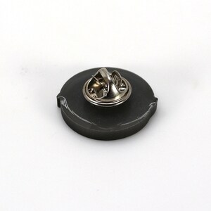 May include: The back of a black metal pin with a silver pin back.