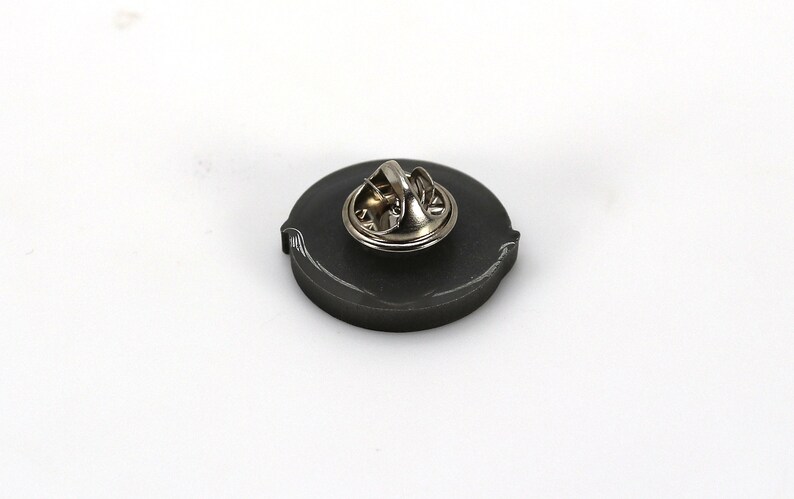 May include: The back of a black metal pin with a silver pin back.