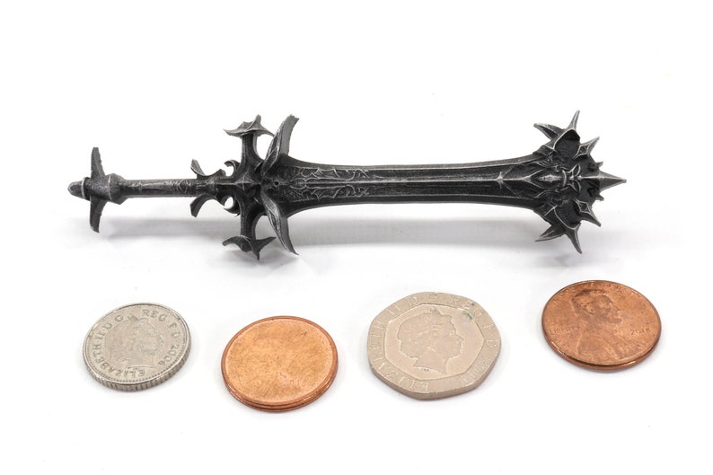 May include: A black metal sword with intricate details, shown next to three coins for scale.