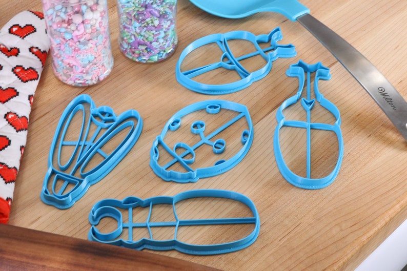 May include: Five blue plastic cookie cutters shaped like ladybugs, a beetle, and a butterfly on a wooden surface.