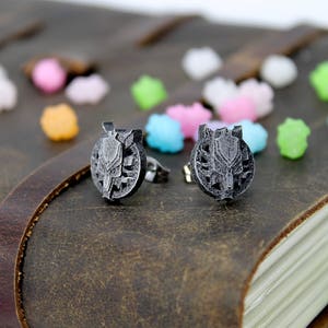 Op de afbeelding: Een paar zilveren oorbel studs met een wolfskop ontwerp. De oorbellen liggen op een bruin lederen oppervlak.