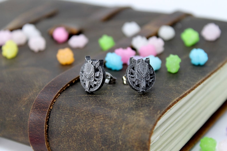 Op de afbeelding: Een paar zilveren oorbel studs met een wolfskop ontwerp. De oorbellen liggen op een bruin lederen oppervlak.